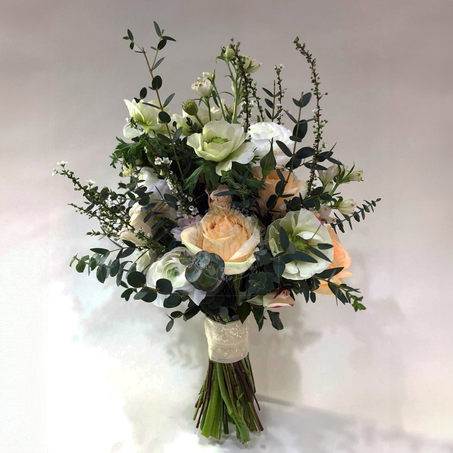 An elegant bridal bouquet with cream roses, white wildflowers, and lush greenery, bound with an ivory lace ribbon.