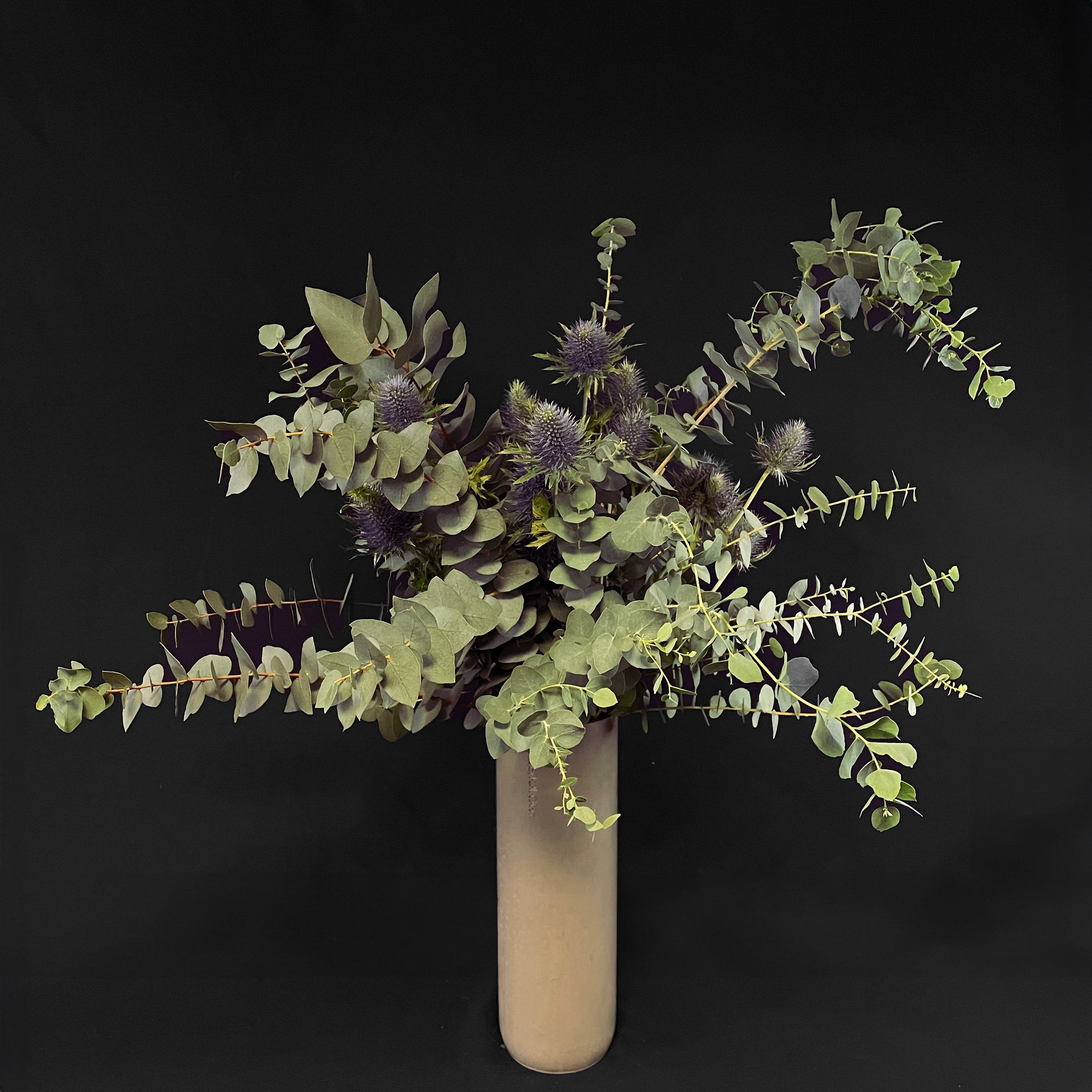 Eucalyptus branches interspersed with spiky Eryngium flowers in a simple vase