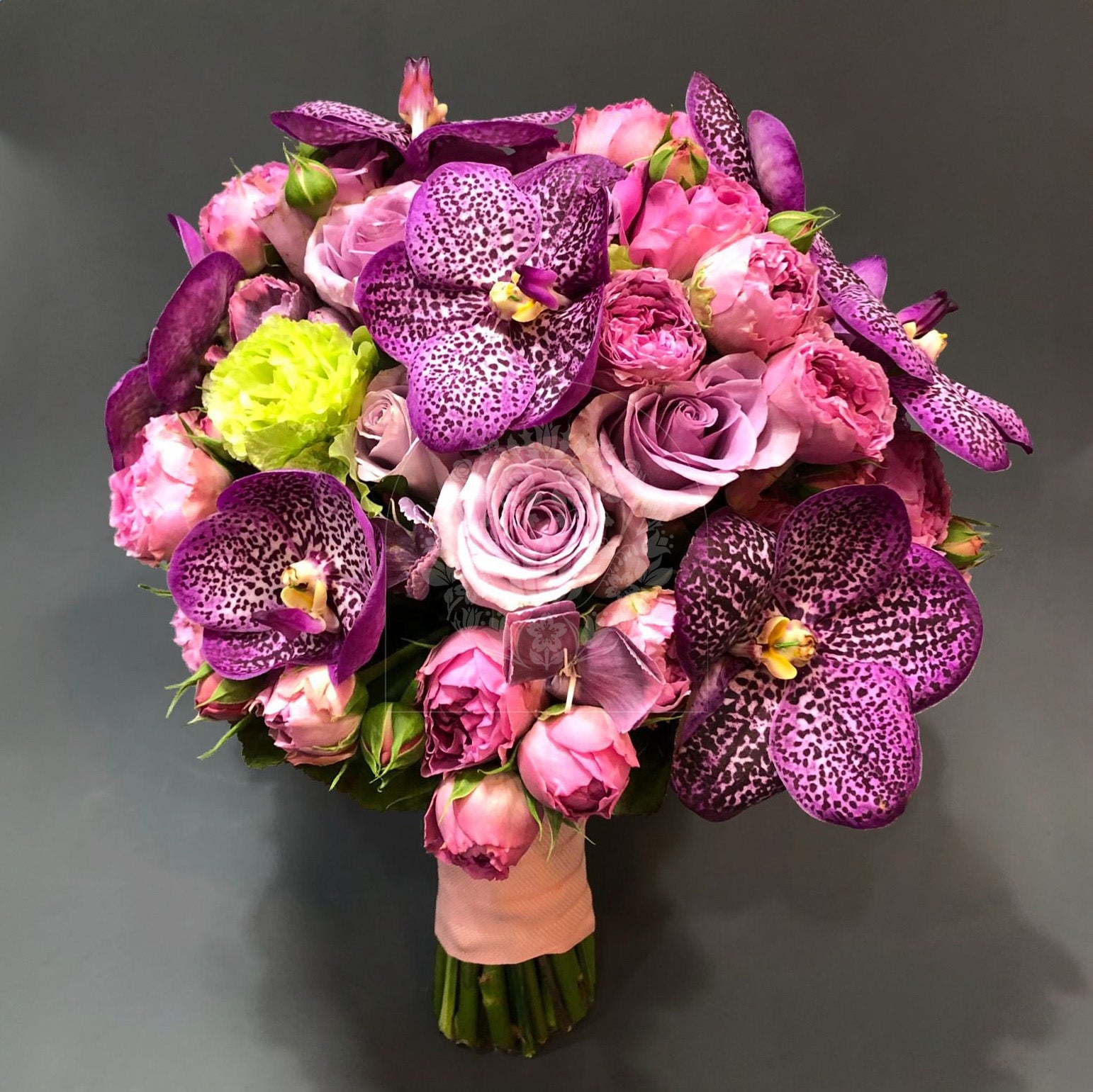 A luxurious bridal bouquet with exotic purple orchids, pink roses, and unique green blooms, all tied with a coral ribbon.