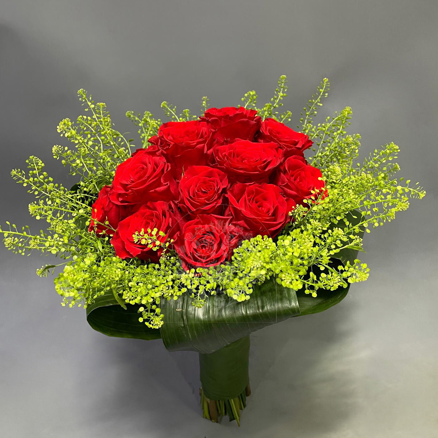 A stunning bridal bouquet composed of vibrant red roses and bright green accents, hand-tied with a broad green leaf wrap.